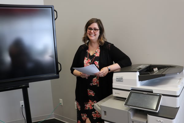 A woman picking up papers from the copier machine.