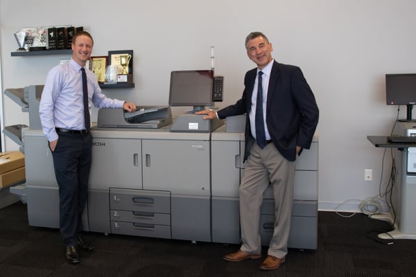 Managed print services professionals smiling beside a large print production unit.